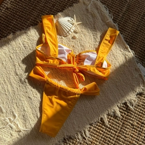 Flat lay of yellow bikini with back bow detail on a beach mat with shells