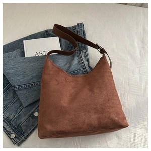 Detailed texture of brown matte suede hobo bag placed on white bedding with a book