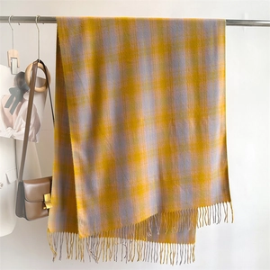 Detail of yellow and grey plaid scarf with soft fringe hanging on a metal rack