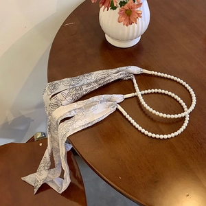 Close-up of pearl chain spliced with black and white floral silk scarf on a wooden table