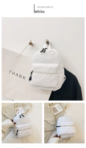 Detail view of a white nylon mini backpack with black zippers and front pocket