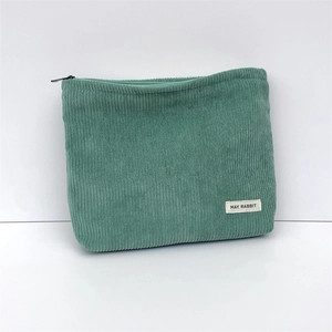 Detail of green corduroy makeup bag featuring soft ribbed texture and a branded fabric label