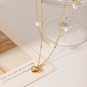 Double-layered gold necklace featuring baroque pearls and a heart pendant on a glass stand