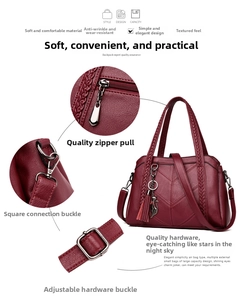 Macro detail of the wine red handbag showing smooth metal zippers and woven handles