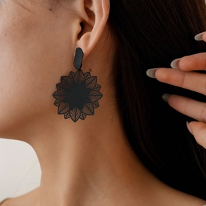 Detail of matte black floral drop earring with intricate hollow petal design on model