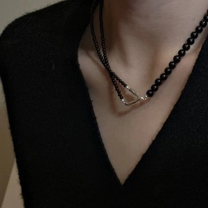 Dettaglio di una collana in argento e perline nere su modella in stile minimalista scuro