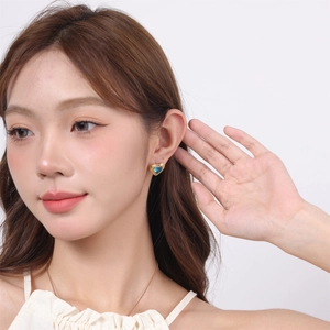 Detail of heart-shaped gold earrings with blue enamel stones worn by a model