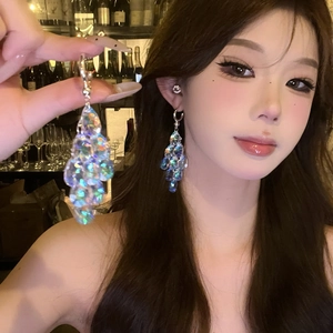 Close-up of long iridescent laser sequin tassel earrings on model in warm bar light
