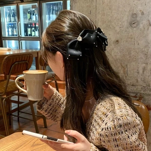 Elegant black bow hair clip with rhinestones worn on long wavy hair in a cafe