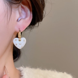Detailed view of model wearing gold heart earrings with white enamel and rhinestones