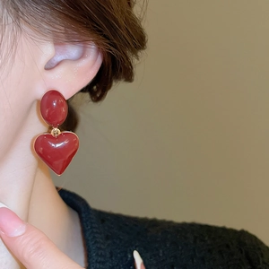 Close-up of elegant red oval and heart-shaped pendant earrings on a model’s ear