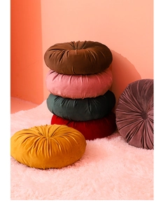Stack of pleated round velvet pumpkin cushions in various colors on a plush pink rug