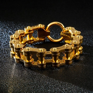 Détail d'un bracelet gourmette en acier doré de style vélo sur cuir noir texturé