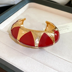 Detail of wide open cuff bracelet with red enamel geometric patterns on gold metal base
