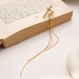 Gold cross sword ear cuff with hanging chains and white rhinestones on vintage book edge