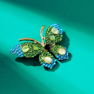 Macro detail of rhinestone butterfly brooch with green gems and gold plating on green base