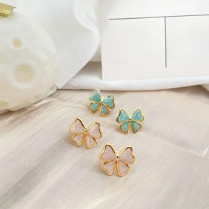 Pink and mint green bow-shaped stud earrings displayed on elegant champagne silk fabric