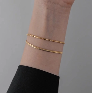 Close-up of double-layered gold snake bone bracelet and textured bead chain on wrist
