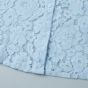 Macro detail of intricate light blue floral lace fabric and matching buttons on the shirt