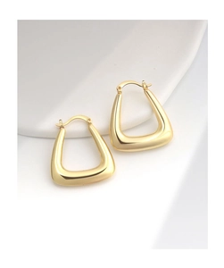 Detailed macro view of high-polished gold U-shaped hollow earrings on white ceramic base