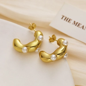Close-up of gold-plated wavy C-shaped hoop earrings with embedded white pearls
