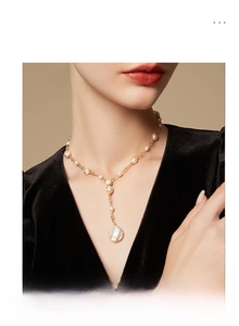 Close-up of elegant Y-shaped gold chain with a large baroque pearl pendant on a model
