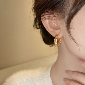 Detail of gold hoop earrings featuring orange and white pavé cubic zirconia on model