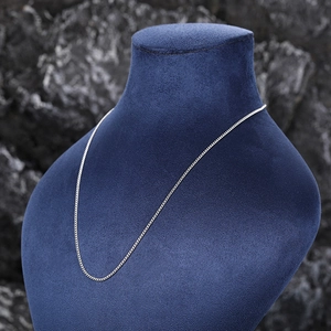 Detail of silver snake chain necklace displayed on blue velvet stand against rock