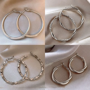 Four styles of silver geometric hoop earrings displayed on elegant silk background
