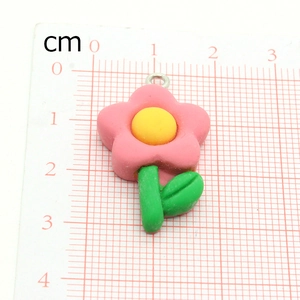 Pink flower charm with green stem and leaves on a centimeter scale measuring board