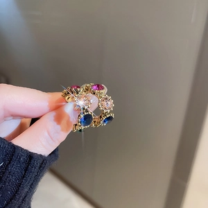 Close-up of gold C-shaped hoop earrings with colorful inlaid rhinestones and gems