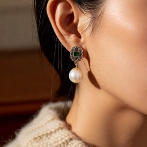 Close-up of vintage style pearl and green gemstone earring worn by a model