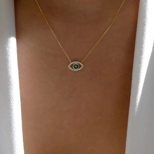 Detail of gold evil eye necklace with green gem and white zircons on female model