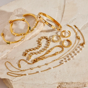 Parure de bijoux dorés en acier inoxydable avec gemmes vertes et perles sur pierre beige