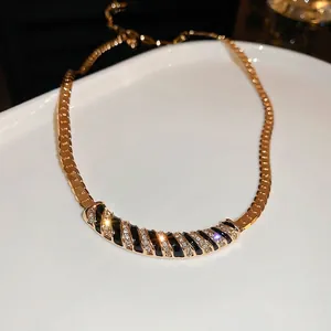 Luxurious gold snake chain necklace with black enamel and diamond-set spiral pendant