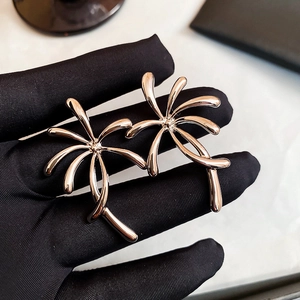 Detailed view of silver palm tree earrings held against a black velvet background