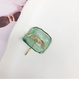 Detailed view of resin U-shaped hair hook with textured green finish and gold metal accents
