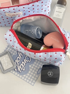 Quilted blue makeup bag with red hearts and zipper, shown open with cosmetics on desk