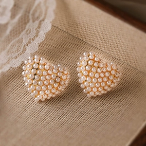 Dettaglio di orecchini a cuore in perle con base dorata su pizzo in stile vintage