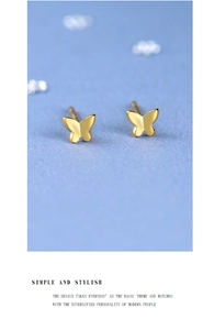 Close-up of minimalist golden butterfly stud earrings on a textured blue surface