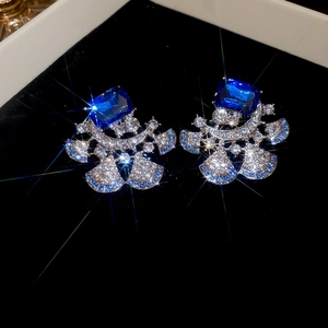 Close-up of luxury flower stud earrings with blue rectangular gemstone and fan-shaped inlay