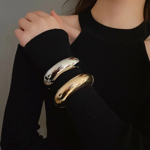 Close-up of wide mirror-polished metal bracelets in gold and silver on a knit sleeve