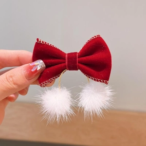 Detail of red velvet bow hair clip with white pom-poms and gold stitching accents