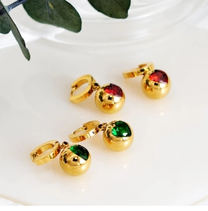 Détail de boucles d'oreilles boules dorées avec zircons cœur en rouge et vert émeraude