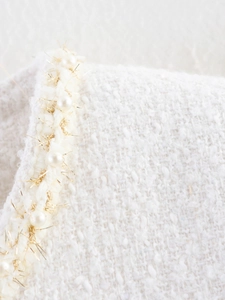 Dettaglio macro di tessuto tweed bianco con finiture in perle e fili metallici d'oro