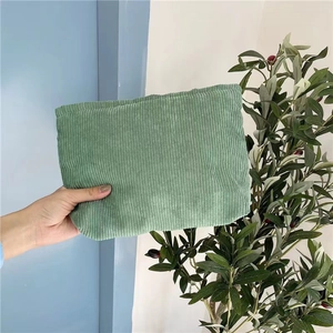 Detail shot of a green corduroy makeup bag held in hand against a blue wall background