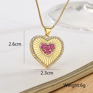 Macro shot of gold heart pendant with pink gemstone and size specs 2.6cm by 2.3cm