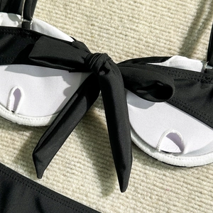 Macro view of textured white bikini fabric featuring a large black bow and fine stitching