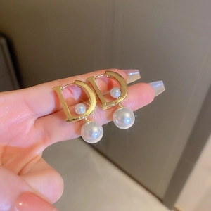 Dettaglio orecchino in metallo dorato a forma di D con perle bianche in mano