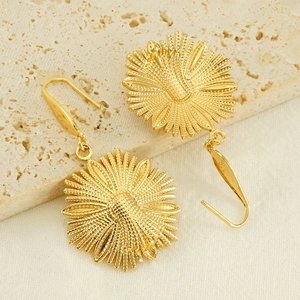 Golden stainless steel sunflower drop earrings with intricate petal texture on stone surface